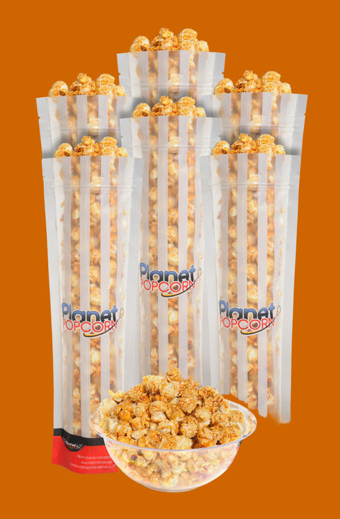 A pack of Caramel Popcorn Little Dipper 6 Pack with visible popcorn inside the packaging. The packaging is predominantly white with red and green accents, and the product name 'PLANET' is visible.