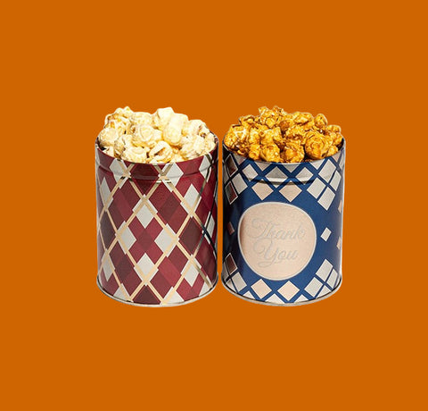 Two cylindrical mini tins, one with a red geometric pattern and the other with a blue and white checkered pattern, both containing popcorn.